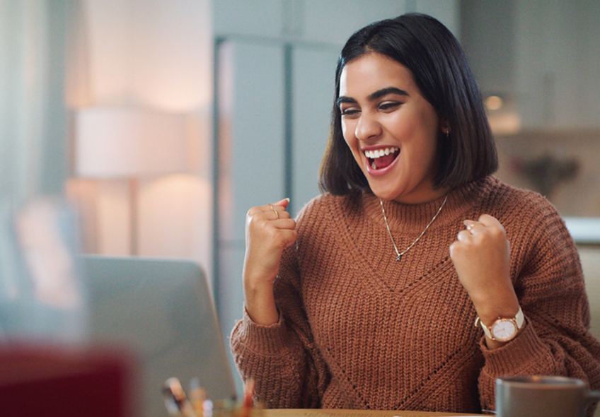 A photo of a young adult female student reacting with a smile to a conversation she is having with someone on her laptop.