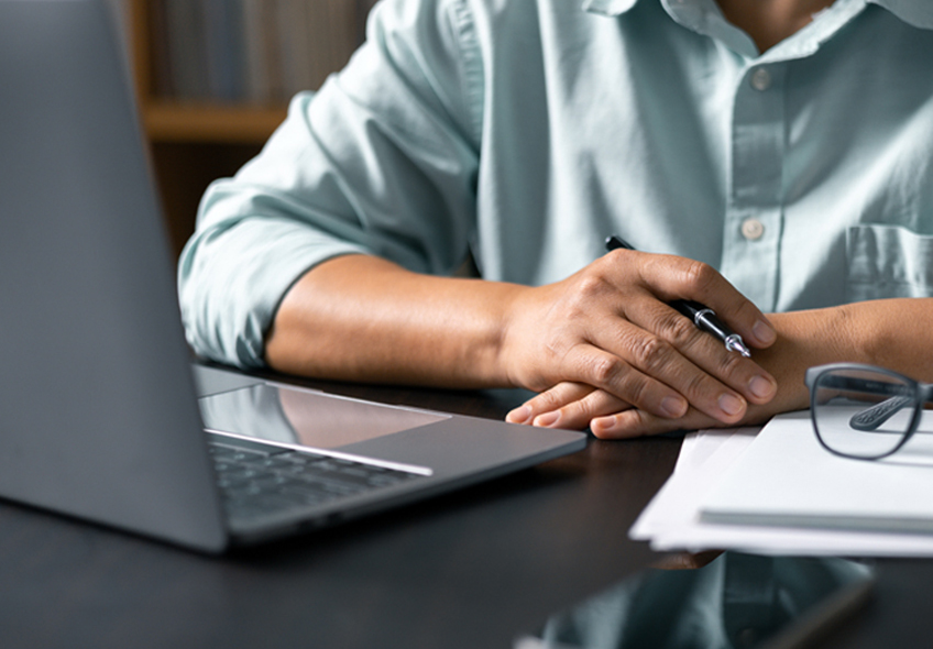 A photo of a person’s arms resting on a table in front of a laptop.
