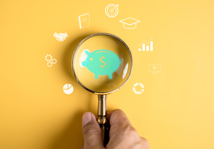 A hand holds a magnifying glass over an image of a green piggy bank. Smaller images are depicted in a circle around the magnifying glass that include a graduation cap, a pie chart, two hands shaking and a target with an arrow in the center.