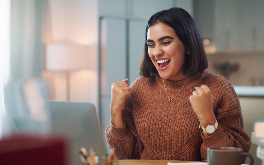 A photo of a young adult female student reacting with a smile to a conversation she is having with someone on her laptop.